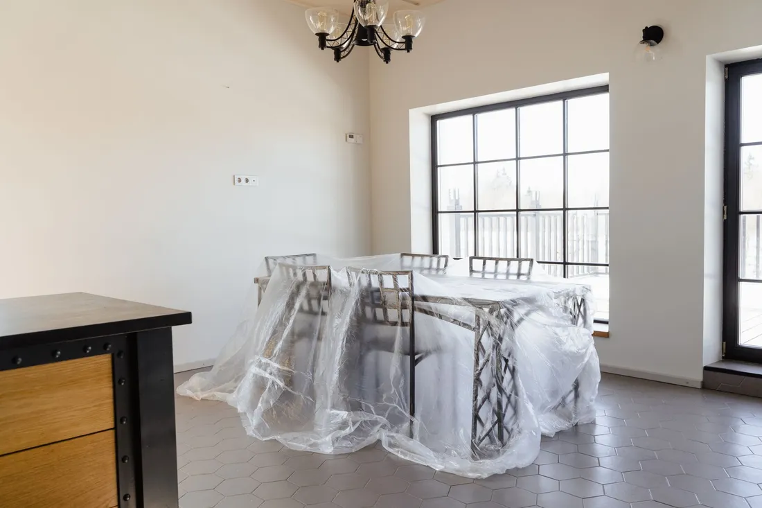Esstisch und Stühle unter einer Schutzfolie in einem ausgeräumten Zimmer